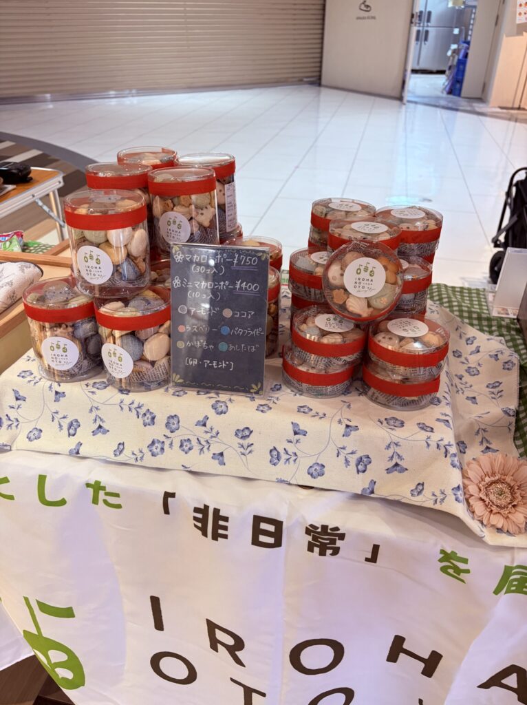 透明の筒型ケースに入れた焼き菓子を積み上げ、卓上に手書きPOPと商品を並べたマルシェブースの近距離の様子。