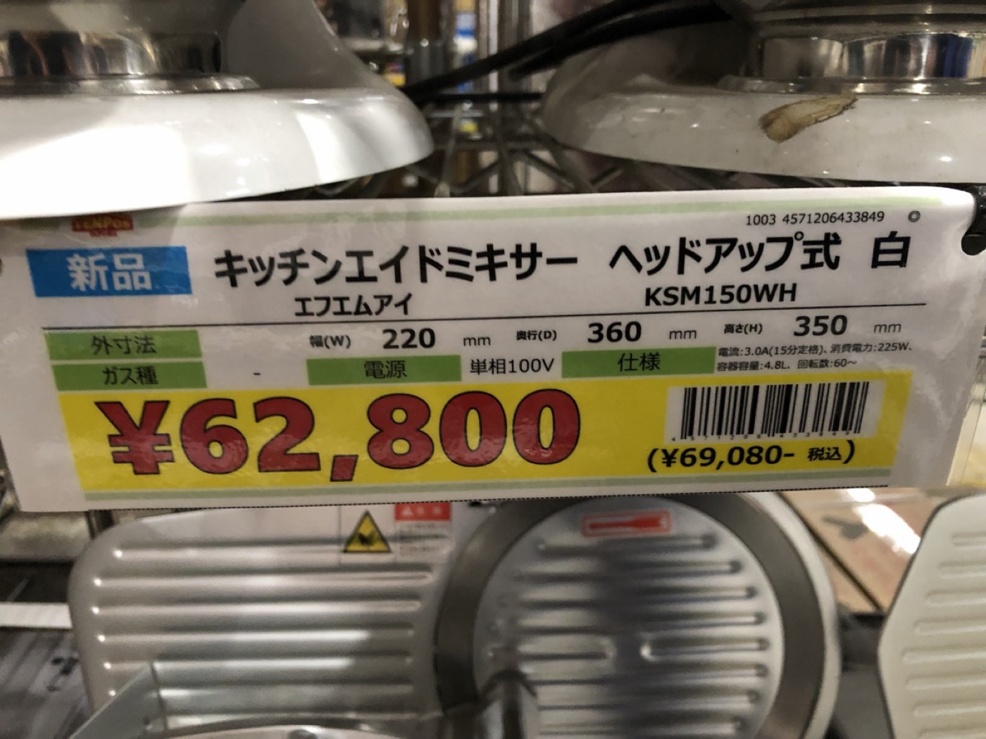 中古厨房機器店に並ぶキッチンエイドミキサーの新品値札。KSM150WH ヘッドアップ式 白、62,800円(税込69,080円)と大きく印字されている。