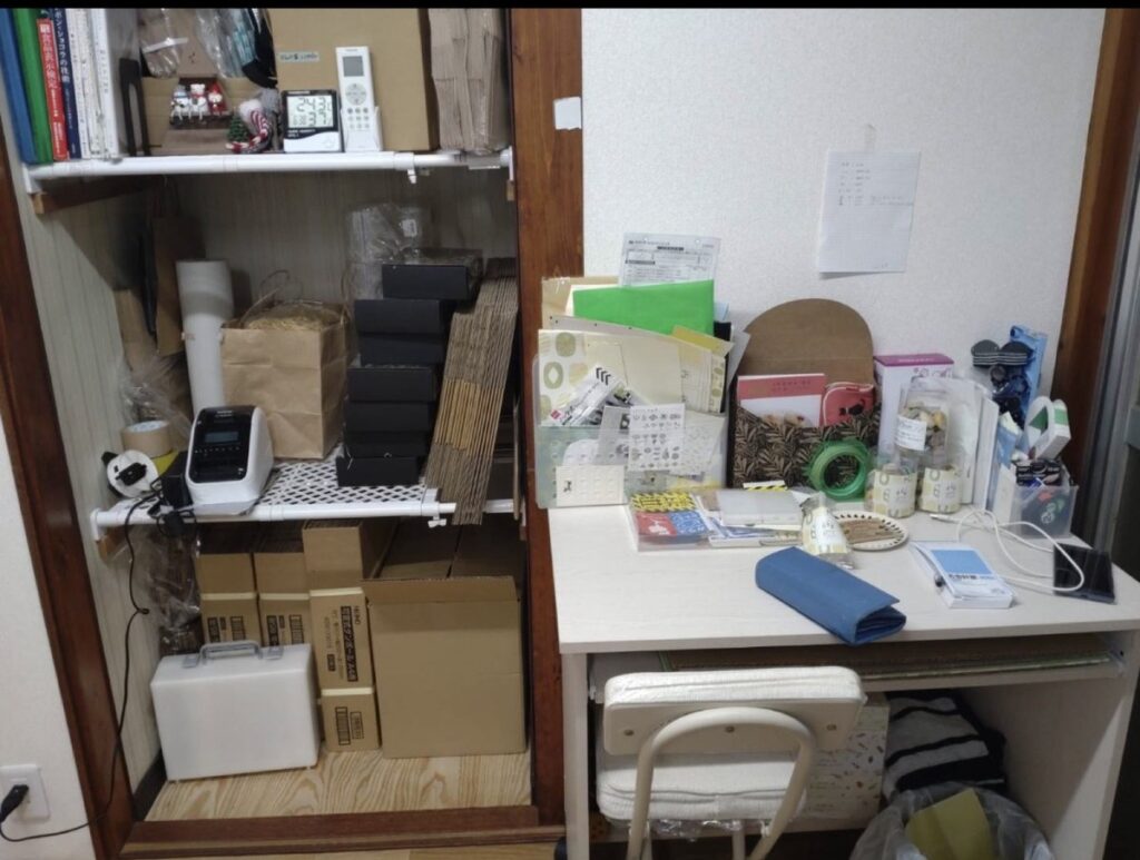 事務机の棚に置いたブラザーのラベルプリンターと、包装資材の在庫の箱。