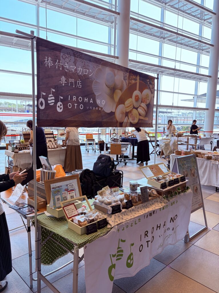 商業施設の中のイベントに出店した、いろはのおとのブース。「棒付きマカロン専門店」の布看板と、焼き菓子を並べた机。