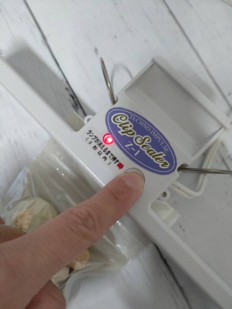 マカロンポーの袋をクリップシーラーではさんでボタンを押し、赤いランプが点いているところ。