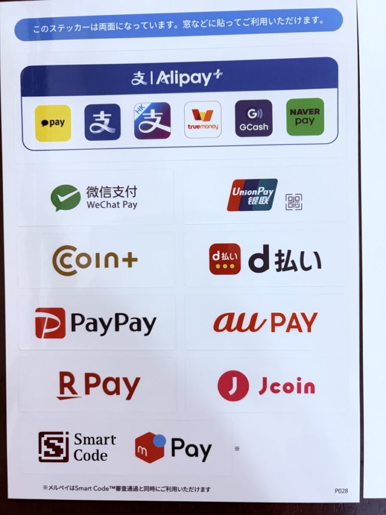 エアペイ経由のQR決済で届いた、窓に貼る両面のロゴステッカー。Alipay+、WeChat Pay、UnionPay、COIN+、d払い、PayPay、au PAY、楽天ペイ、J-Coin Pay、Smart Code、メルペイのロゴが並んでいる（2026年10月）