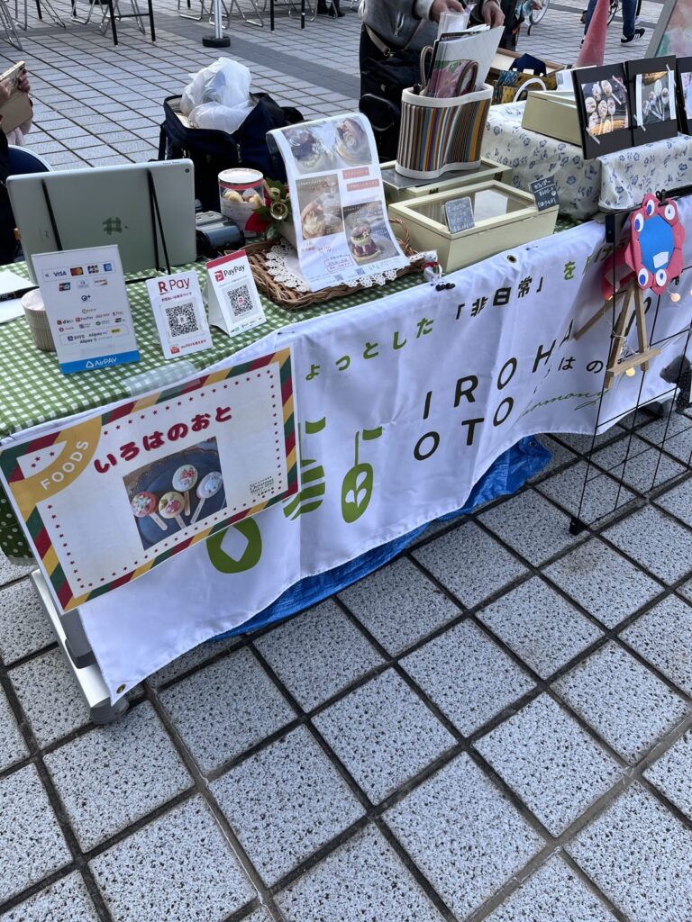 2025年12月の屋外マルシェのブース。テーブル正面にタペストリーを掛け、手前に支払い方法の案内を並べている。