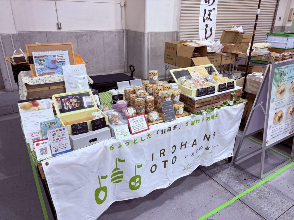 2026年7月の神戸ハンドメイドマルシェのブース。正面のタペストリー、木の台で高さを出した商品、右のA型看板。