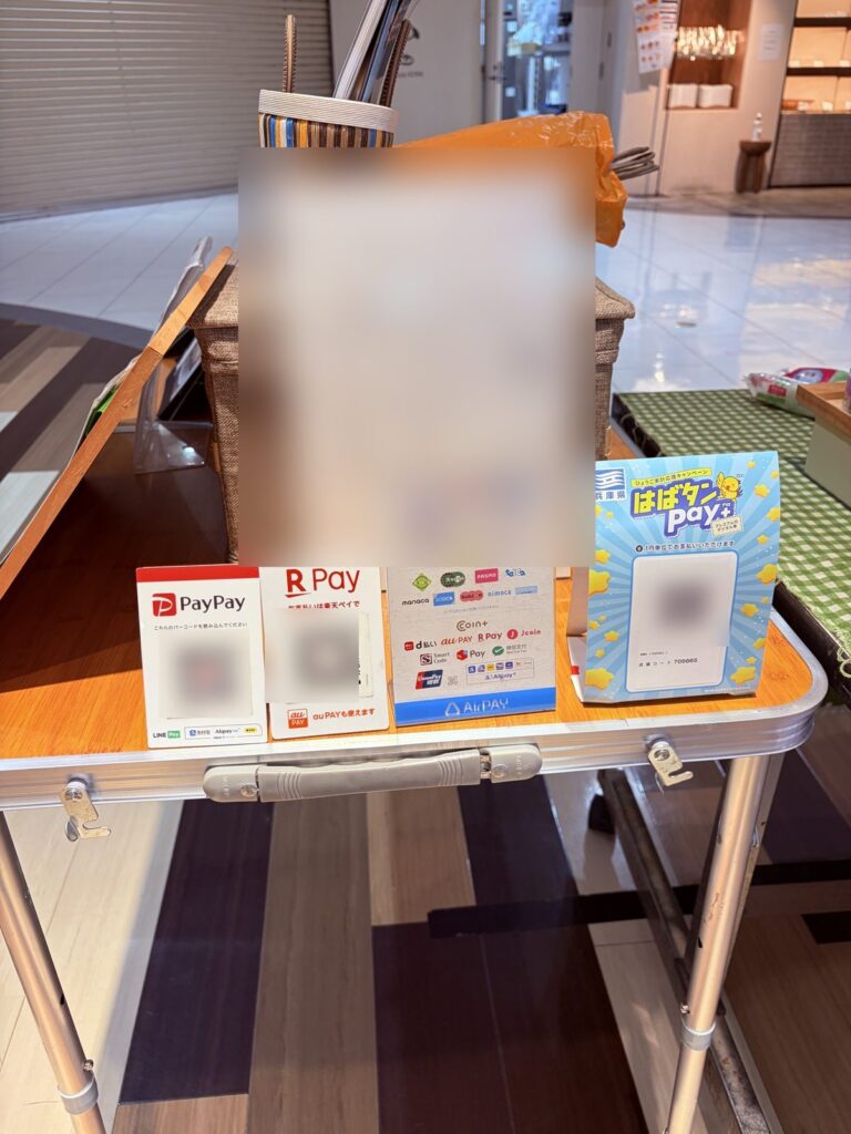 マルシェの折りたたみテーブルに並べた、PayPay・楽天ペイ・エアペイ・はばタンPay+の案内（QRコードはぼかしています）